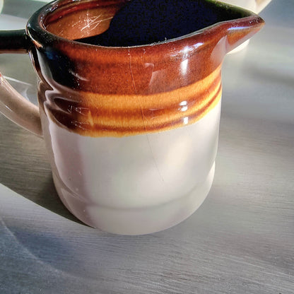 Vintage ceramic measuring jug set with caramel glaze and blue cup markings, including one cracked jug, styled on a table.