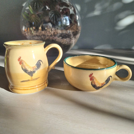 Ceramic rooster mug and cup set in warm yellow tones, styled on a tabletop in natural light.