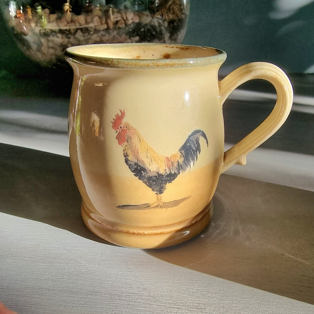 Ceramic rooster mug and cup set in warm yellow tones, styled on a tabletop in natural light.