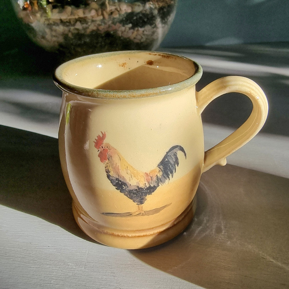 Ceramic rooster mug and cup set in warm yellow tones, styled on a tabletop in natural light.