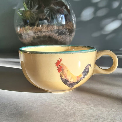 Ceramic rooster mug and cup set in warm yellow tones, styled on a tabletop in natural light.