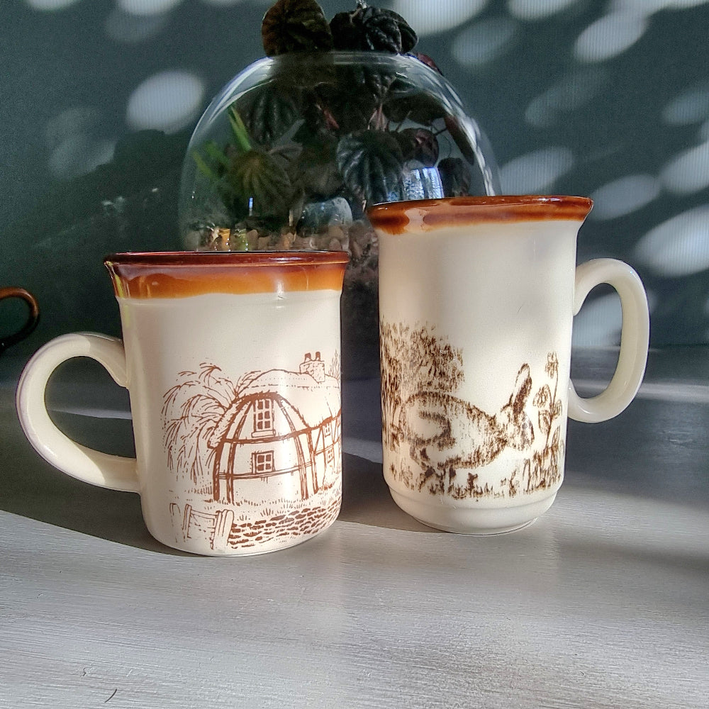 Two vintage English mugs by Bilton and Churchill with rabbit and cottage countryside illustrations on a tabletop.