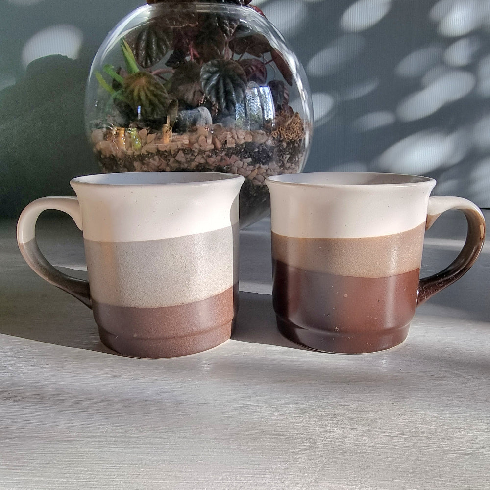 Stoneware mug pair with layered grey and neutral glaze, photographed on a tabletop in natural light.
