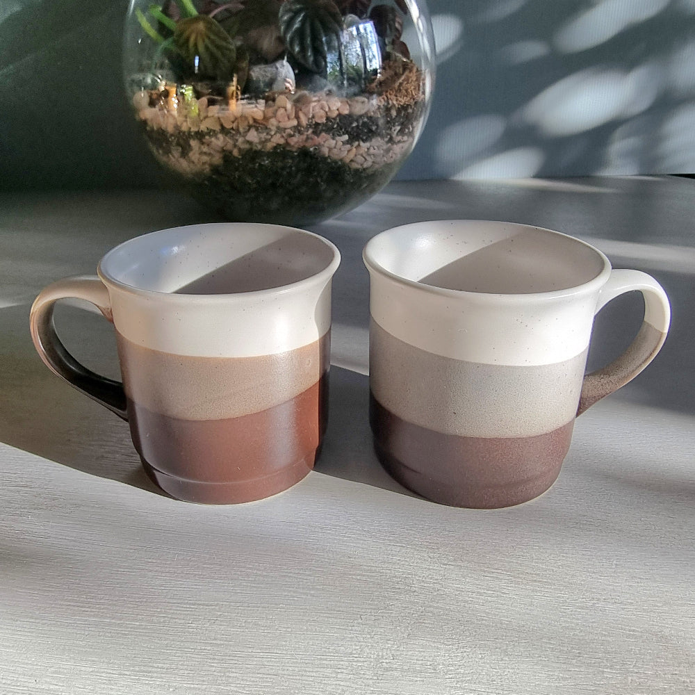 Stoneware mug pair with layered grey and neutral glaze, photographed on a tabletop in natural light.