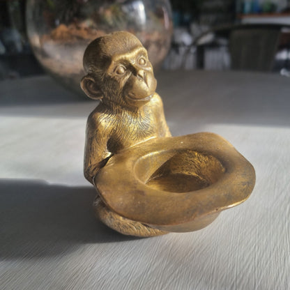 Small gold monkey tealight holder with antique brass-style finish holding candle dish.