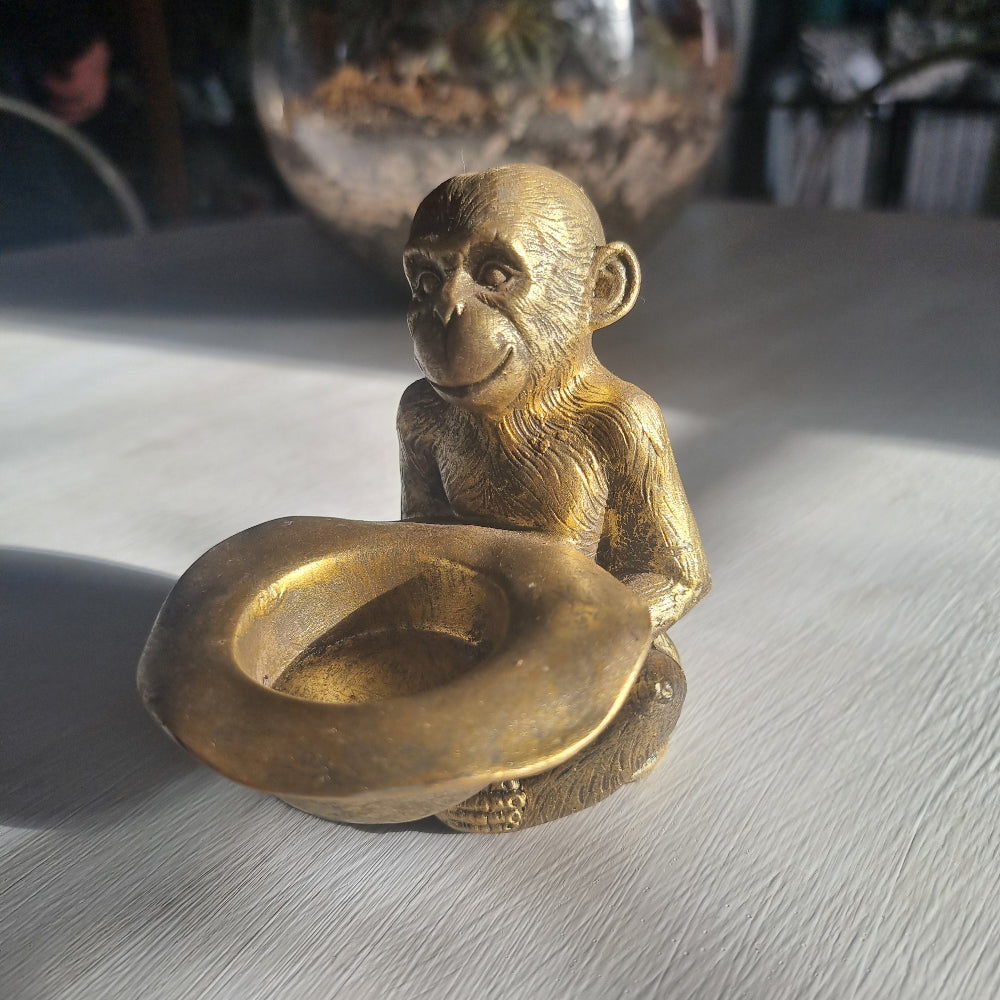 Small gold monkey tealight holder with antique brass-style finish holding candle dish.