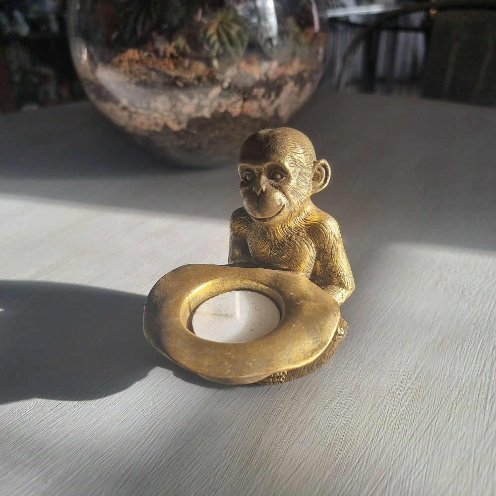 Small gold monkey tealight holder with antique brass-style finish holding candle dish.