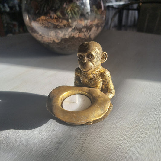 Small gold monkey tealight holder with antique brass-style finish holding candle dish.