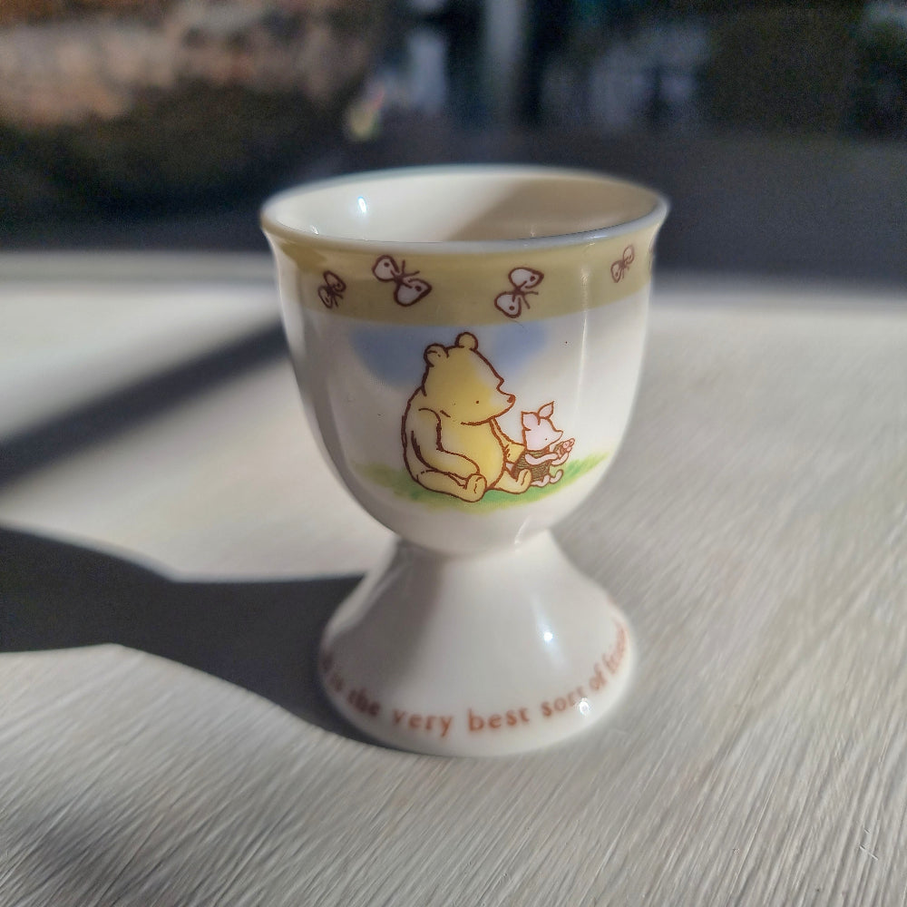 Winnie the Pooh egg cup with butterfly border and pedestal base featuring Pooh illustration.