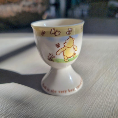 Winnie the Pooh egg cup with butterfly border and pedestal base featuring Pooh illustration.