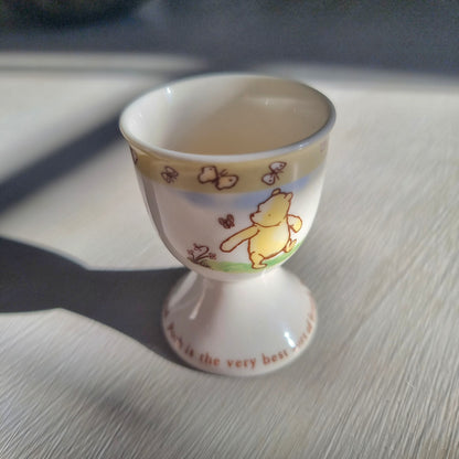 Winnie the Pooh egg cup with butterfly border and pedestal base featuring Pooh illustration.