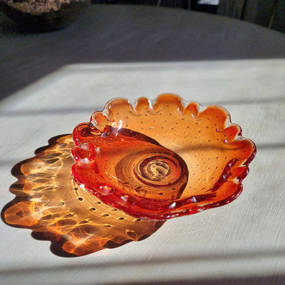 Amber art glass dish with ruffled edge and bubble detail catching warm sunlight