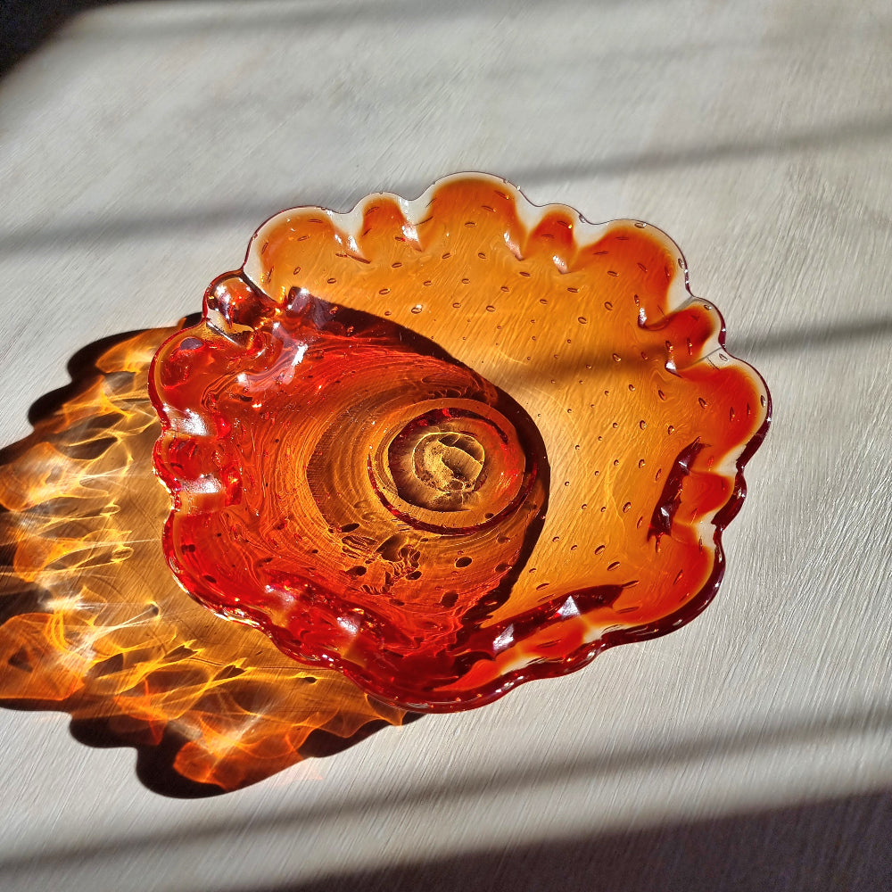 Amber art glass dish with ruffled edge and bubble detail catching warm sunlight