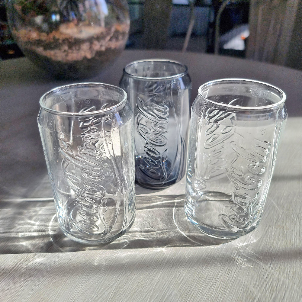 Three Coca-Cola can-shaped drinking glasses with embossed Coke logo, two clear and one smoky glass.