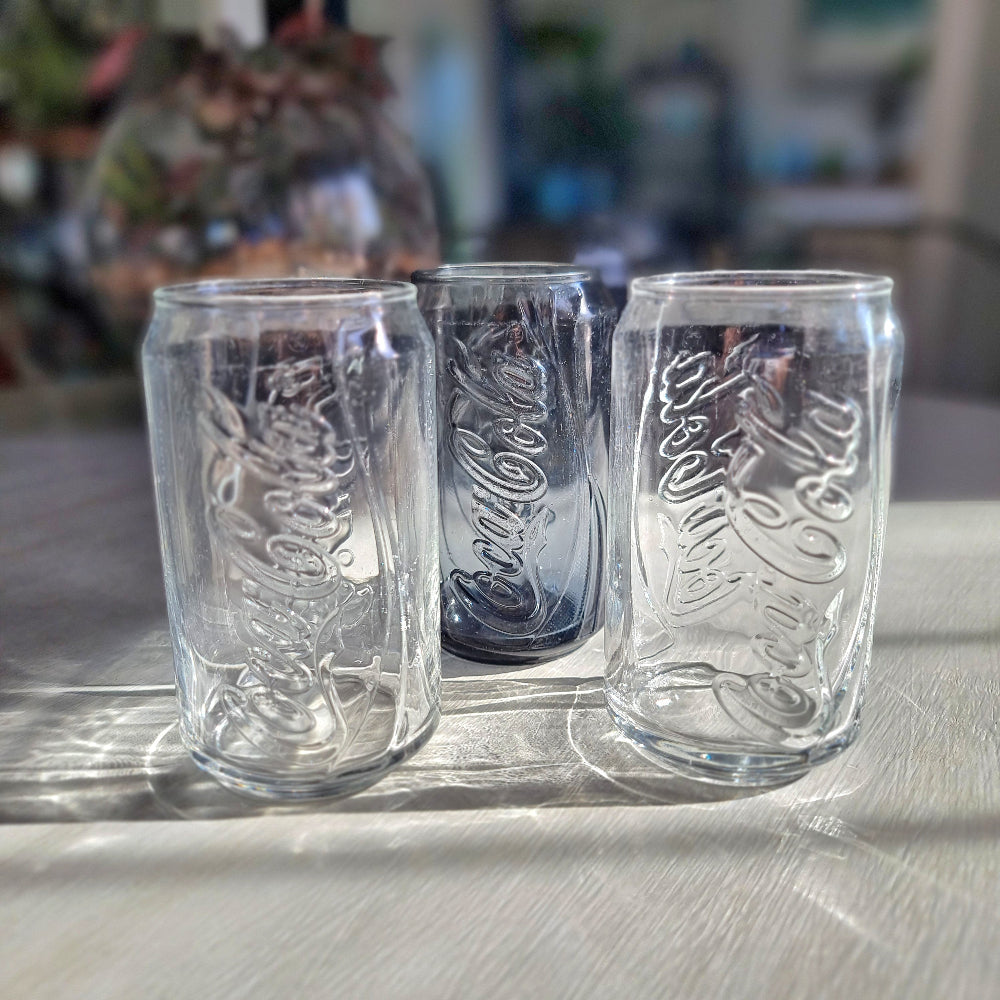 Three Coca-Cola can-shaped drinking glasses with embossed Coke logo, two clear and one smoky glass.