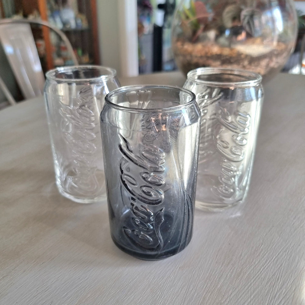 Three Coca-Cola can-shaped drinking glasses with embossed Coke logo, two clear and one smoky glass.