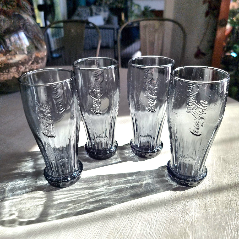 Set of four smoky grey Coca-Cola contour glasses with embossed logo and bottle cap style base.