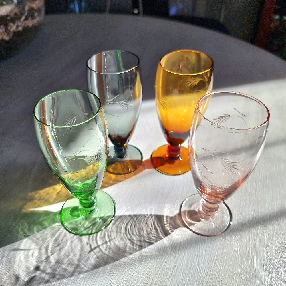 Set of four coloured champagne flutes in green, amber, blue and pink with etched pattern