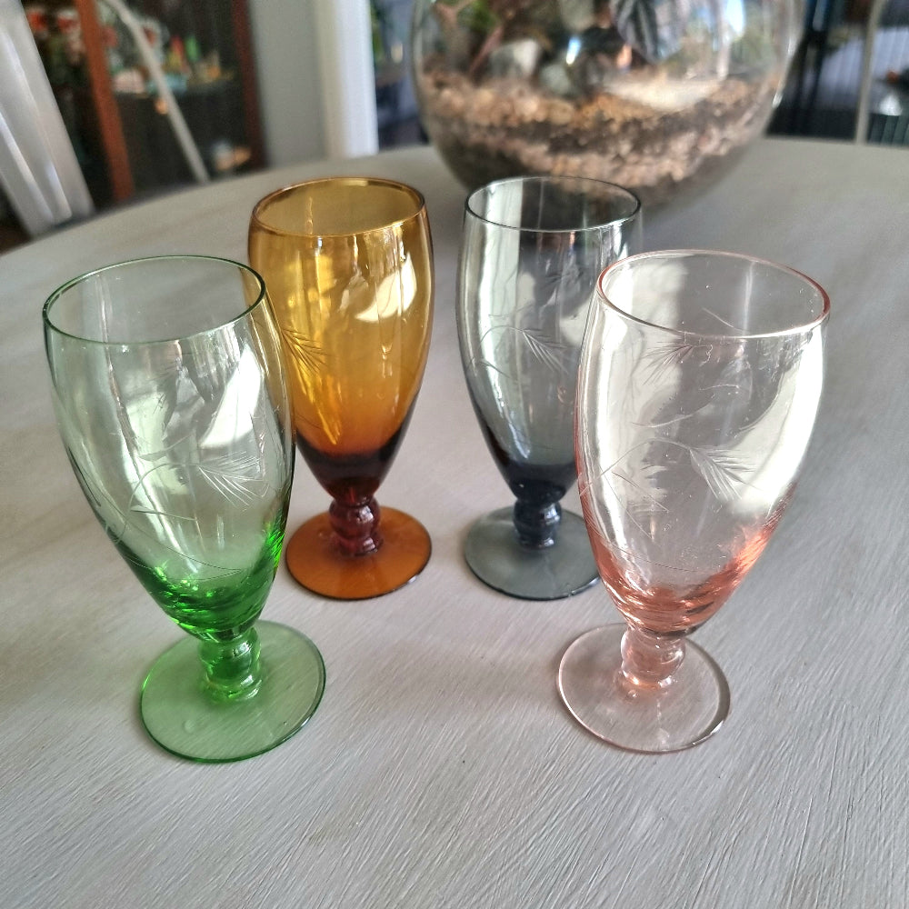 Set of four coloured champagne flutes in green, amber, blue and pink with etched pattern