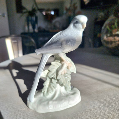 Vintage porcelain budgerigar figurine in glossy white glaze perched on a branch with sculpted leaf base