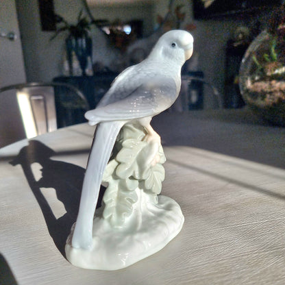 Vintage porcelain budgerigar figurine in glossy white glaze perched on a branch with sculpted leaf base