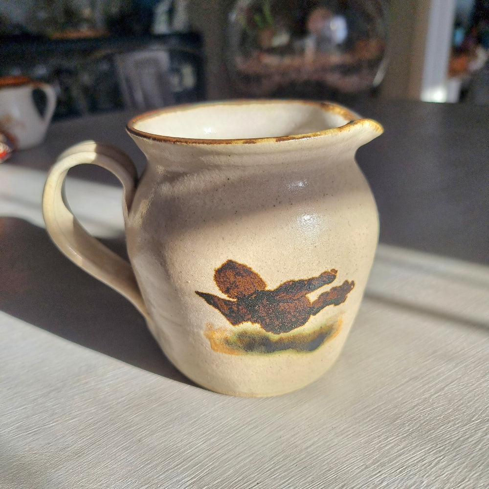 Vintage studio pottery cream jug with speckled sandy glaze and abstract brushwork