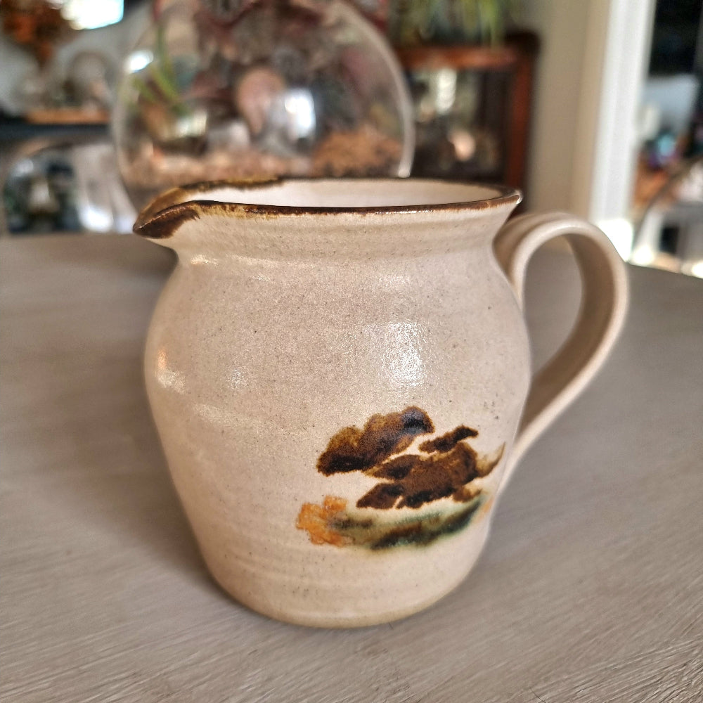 Vintage studio pottery cream jug with speckled sandy glaze and abstract brushwork