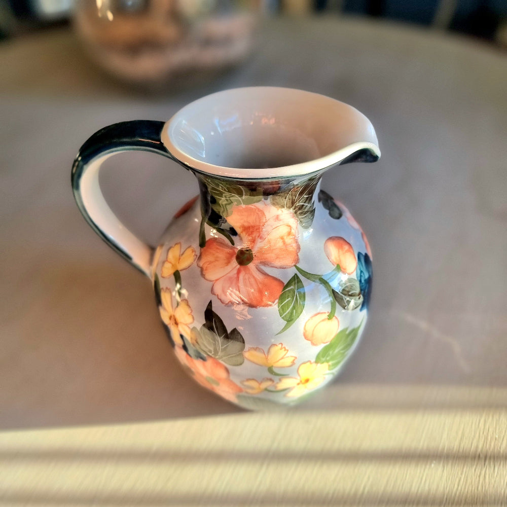 Large vintage hand-painted ceramic jug with pink and yellow floral design on periwinkle white glaze, forest green handle and neck trim