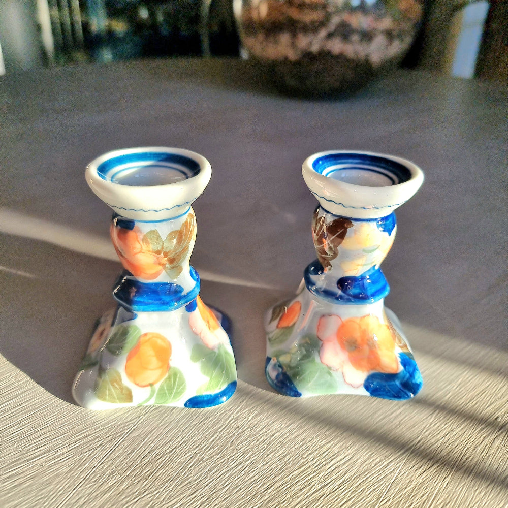 Pair of vintage hand-painted ceramic candlestick holders with orange peach and pink floral design on white glaze with cobalt blue brushstrokes and trim, flared square base