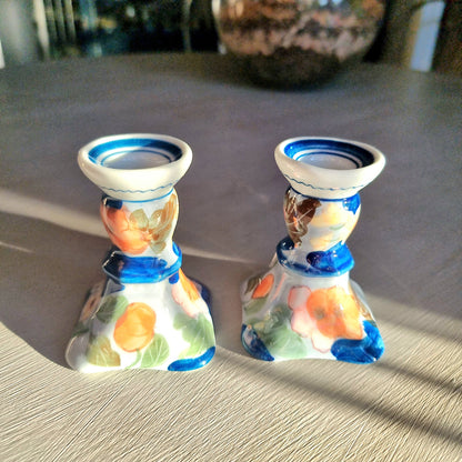 Pair of vintage hand-painted ceramic candlestick holders with orange peach and pink floral design on white glaze with cobalt blue brushstrokes and trim, flared square base