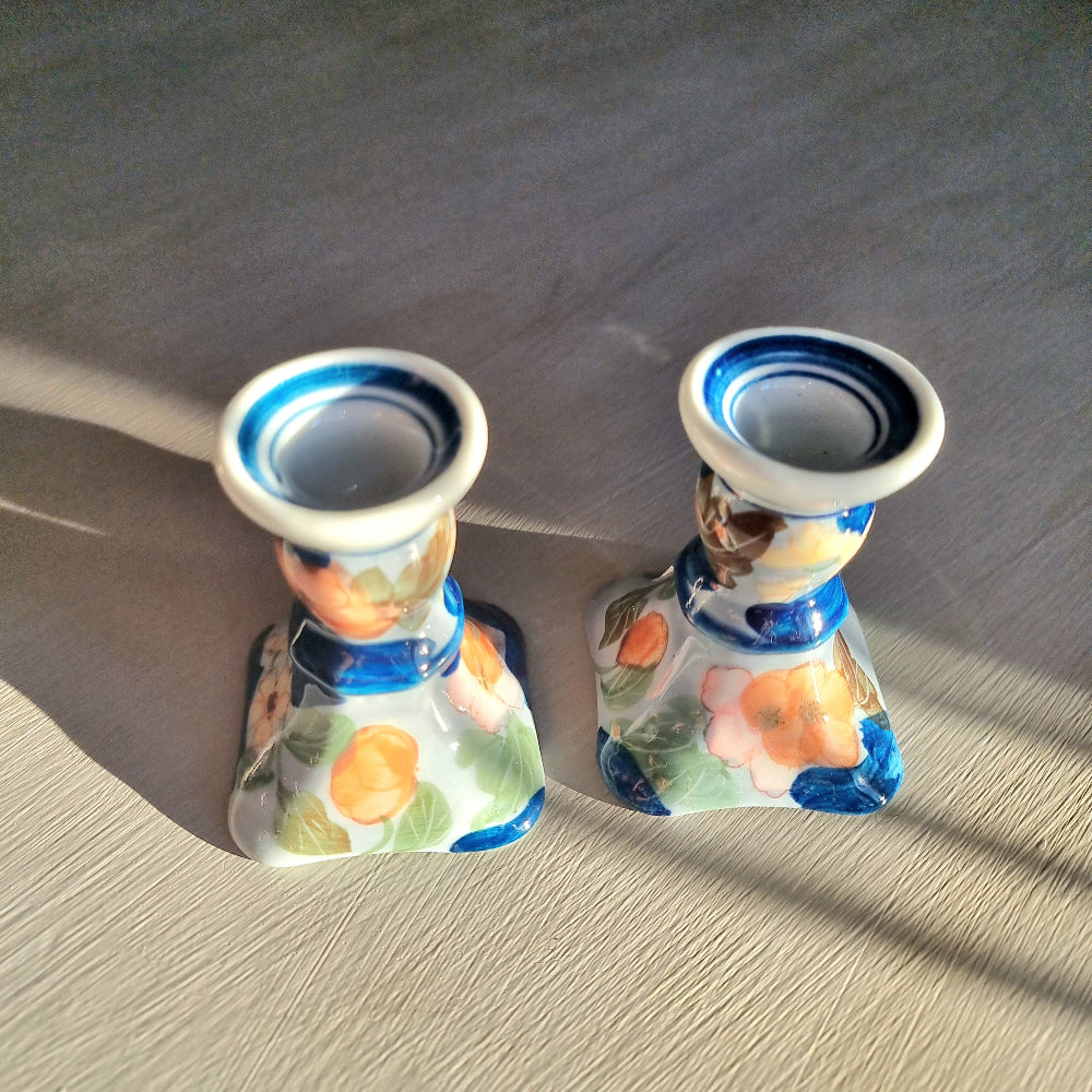 Pair of vintage hand-painted ceramic candlestick holders with orange peach and pink floral design on white glaze with cobalt blue brushstrokes and trim, flared square base