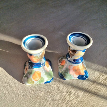 Pair of vintage hand-painted ceramic candlestick holders with orange peach and pink floral design on white glaze with cobalt blue brushstrokes and trim, flared square base