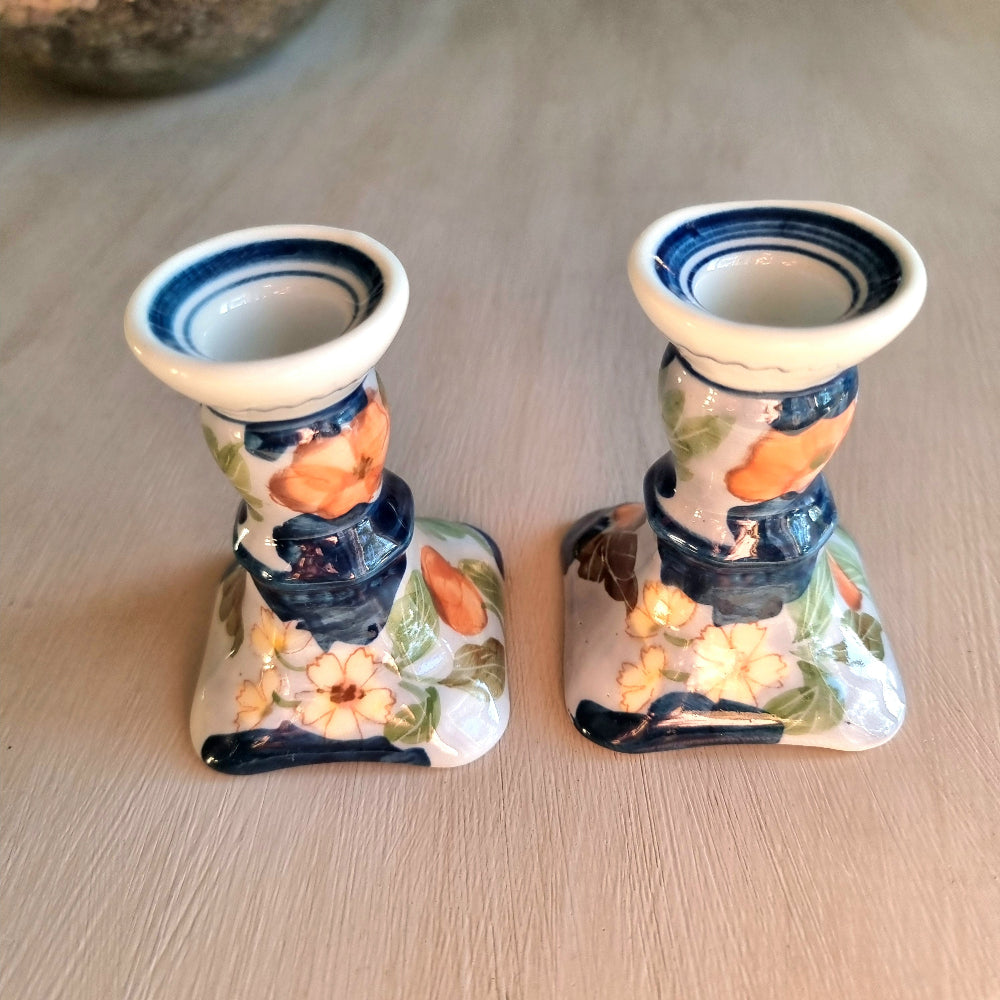 Pair of vintage hand-painted ceramic candlestick holders with orange peach and pink floral design on white glaze with cobalt blue brushstrokes and trim, flared square base