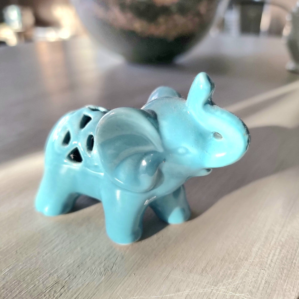 Turquoise glazed ceramic elephant figurine with raised trunk and pierced lattice cutout detail on its back, standing pose on a light wooden surface