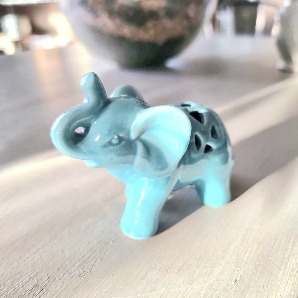 Turquoise glazed ceramic elephant figurine with raised trunk and pierced lattice cutout detail on its back, standing pose on a light wooden surface