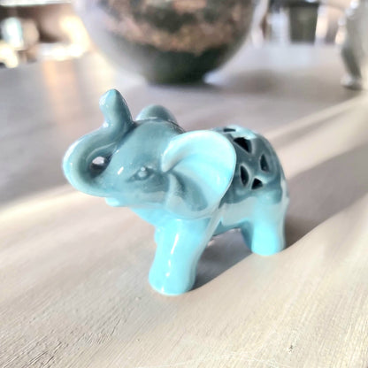 Turquoise glazed ceramic elephant figurine with raised trunk and pierced lattice cutout detail on its back, standing pose on a light wooden surface
