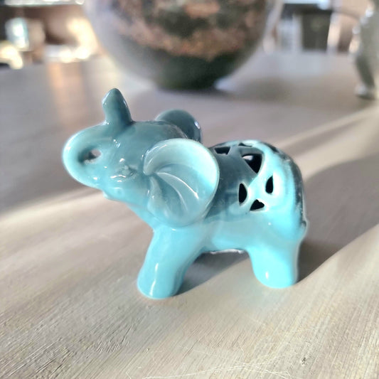 Turquoise glazed ceramic elephant figurine with raised trunk and pierced lattice cutout detail on its back, standing pose on a light wooden surface