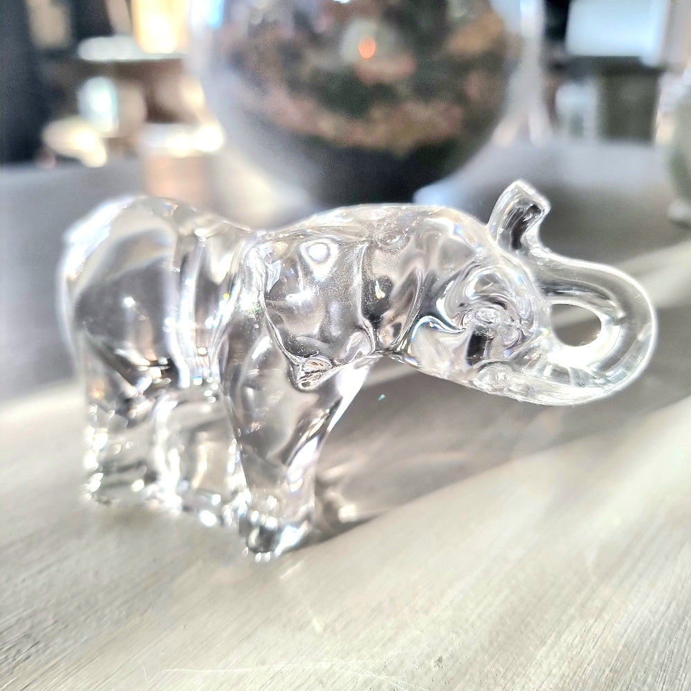 Villeroy and Boch clear crystal glass elephant figurine with raised trunk in walking pose, refracting light on a pale wooden surface