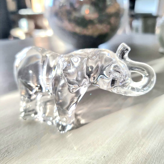 Villeroy and Boch clear crystal glass elephant figurine with raised trunk in walking pose, refracting light on a pale wooden surface