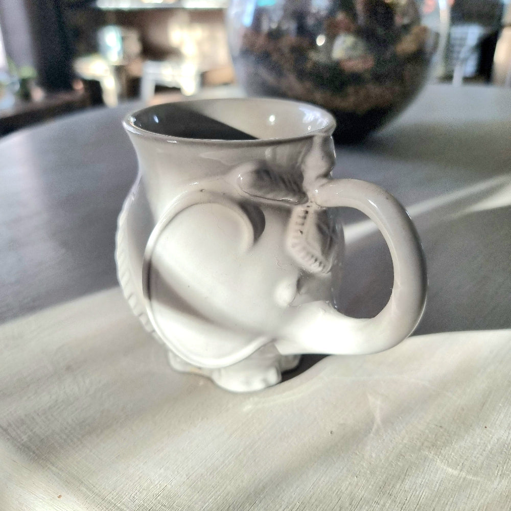 Jonathan Adler Utopia white stoneware elephant mug with trunk spout and tail handle, glossy glaze, viewed from the side on a pale surface