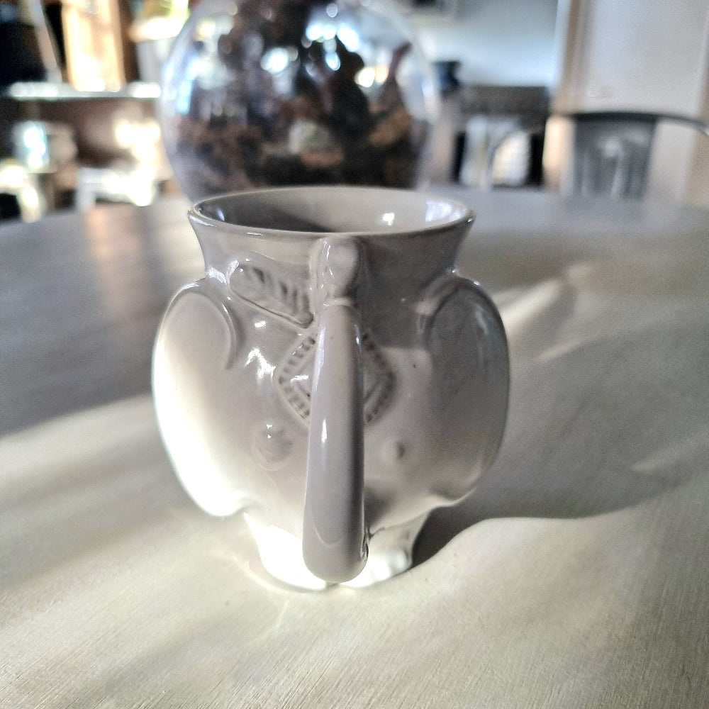 Jonathan Adler Utopia white stoneware elephant mug with trunk spout and tail handle, glossy glaze, viewed from the side on a pale surface