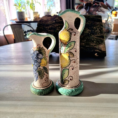 Pair of hand-painted Deruta-style ceramic jug vases with grape and lemon motifs, on wooden bases