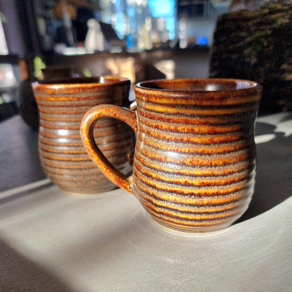 Pair of vintage ribbed mugs with amber and brown drip glaze, one with a small glaze nick on the rim