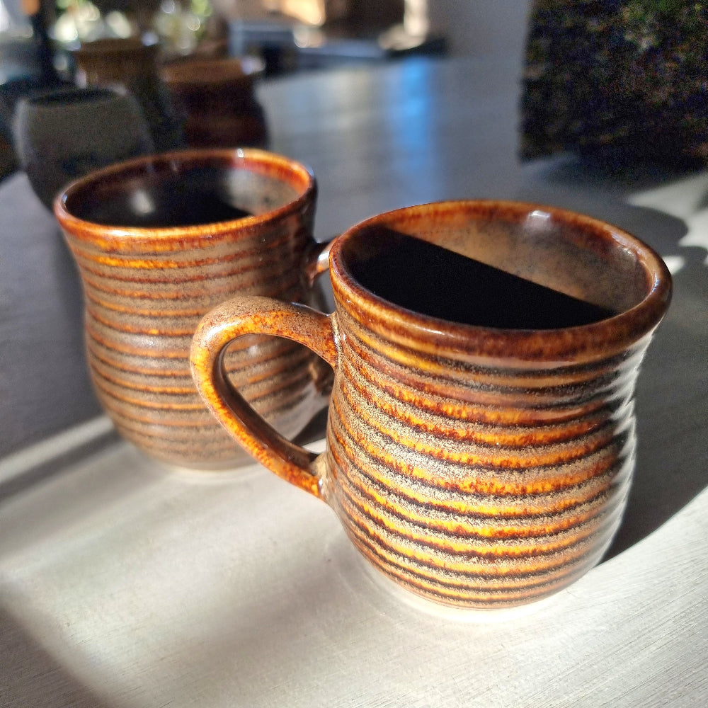 Pair of vintage ribbed mugs with amber and brown drip glaze, one with a small glaze nick on the rim