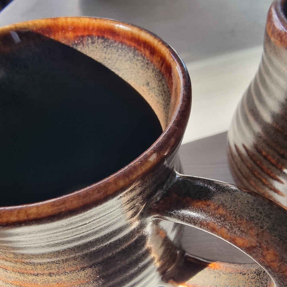 Pair of vintage ribbed mugs with amber and brown drip glaze, one with a small glaze nick on the rim