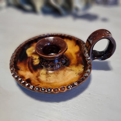 Vintage ceramic chamberstick candle holder with mottled brown and amber glaze, beaded rim, and ring handle