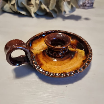 Vintage ceramic chamberstick candle holder with mottled brown and amber glaze, beaded rim, and ring handle