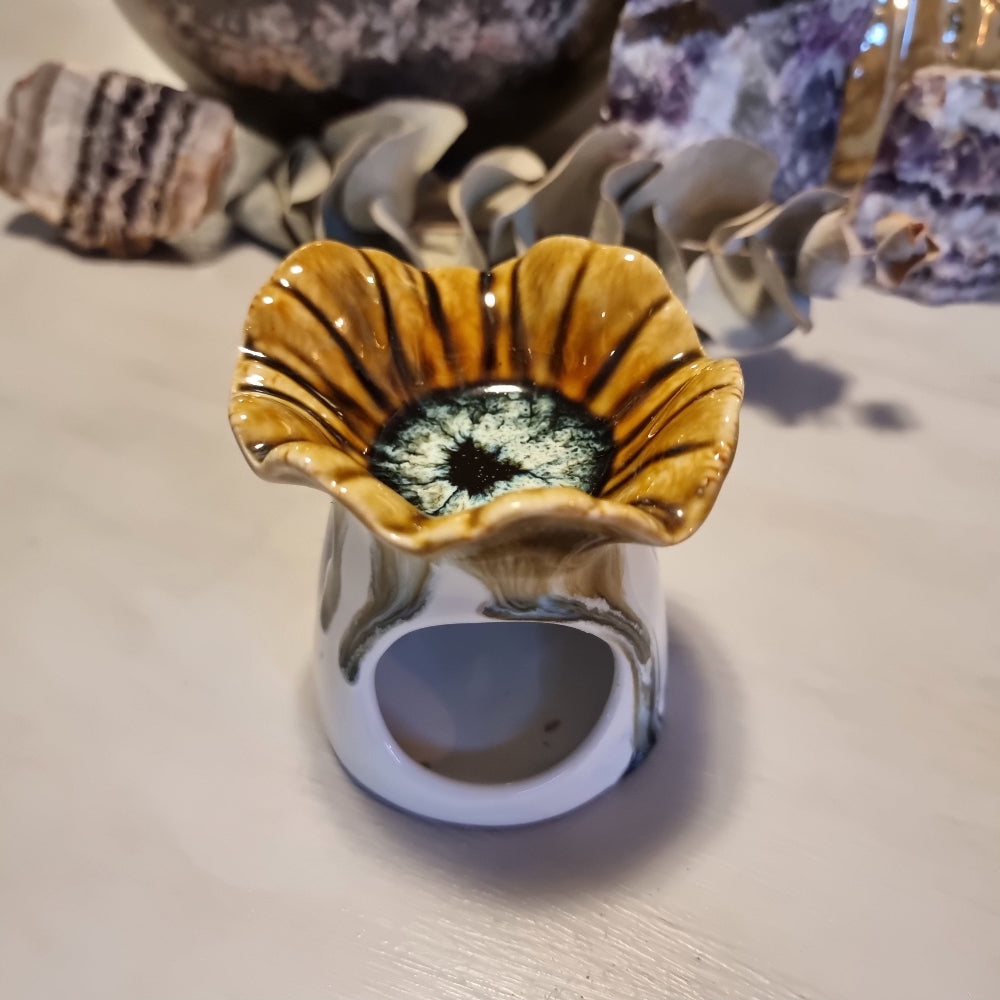 Ceramic oil burner with scalloped flower-shaped top in honey and amber striped glaze, on a white cylindrical base with heat vent