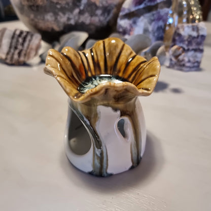 Ceramic oil burner with scalloped flower-shaped top in honey and amber striped glaze, on a white cylindrical base with heat vent