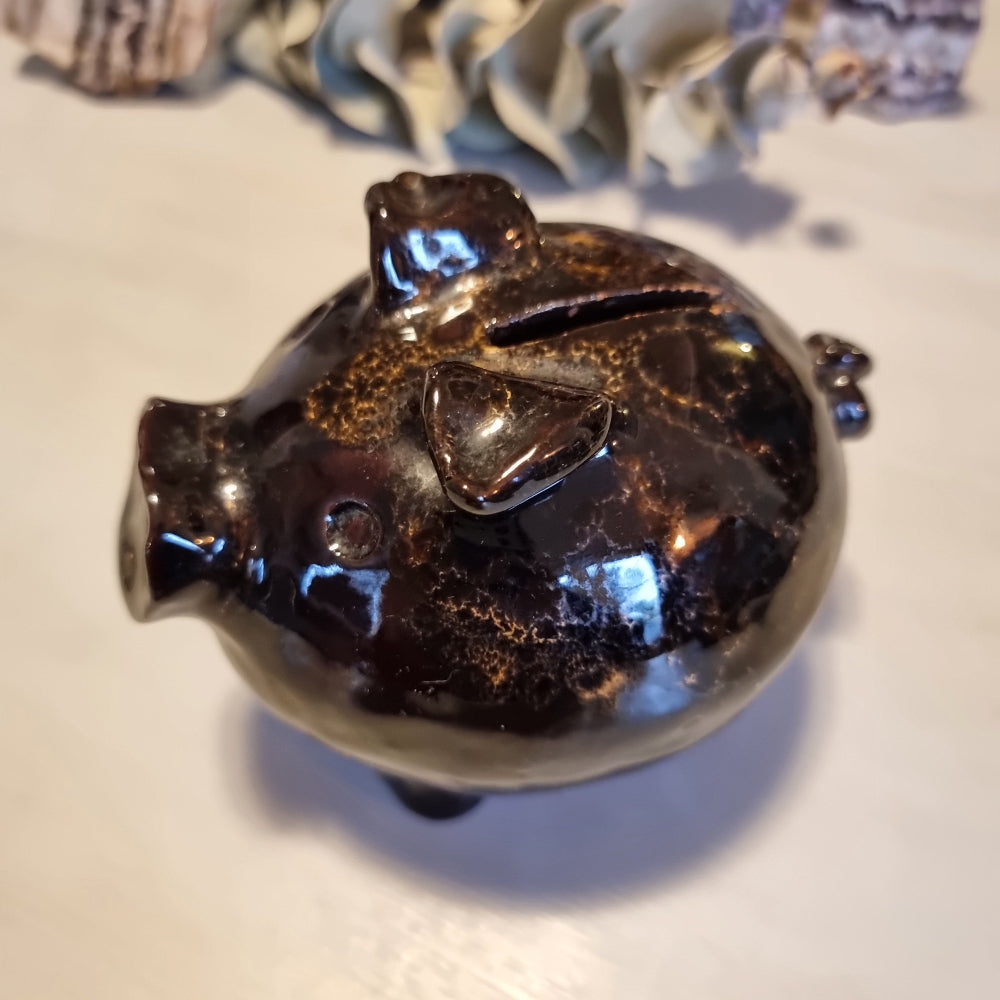 Vintage ceramic piggy money box in mottled brown glaze with speckled highlights, standing on four legs with a coin slot